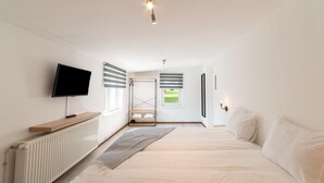 A modern bedroom with a large bed, a TV mounted on the wall, a radiator, and a window with blinds. - Pet Friendly Villa in Elsenborn (Buetgenbach)