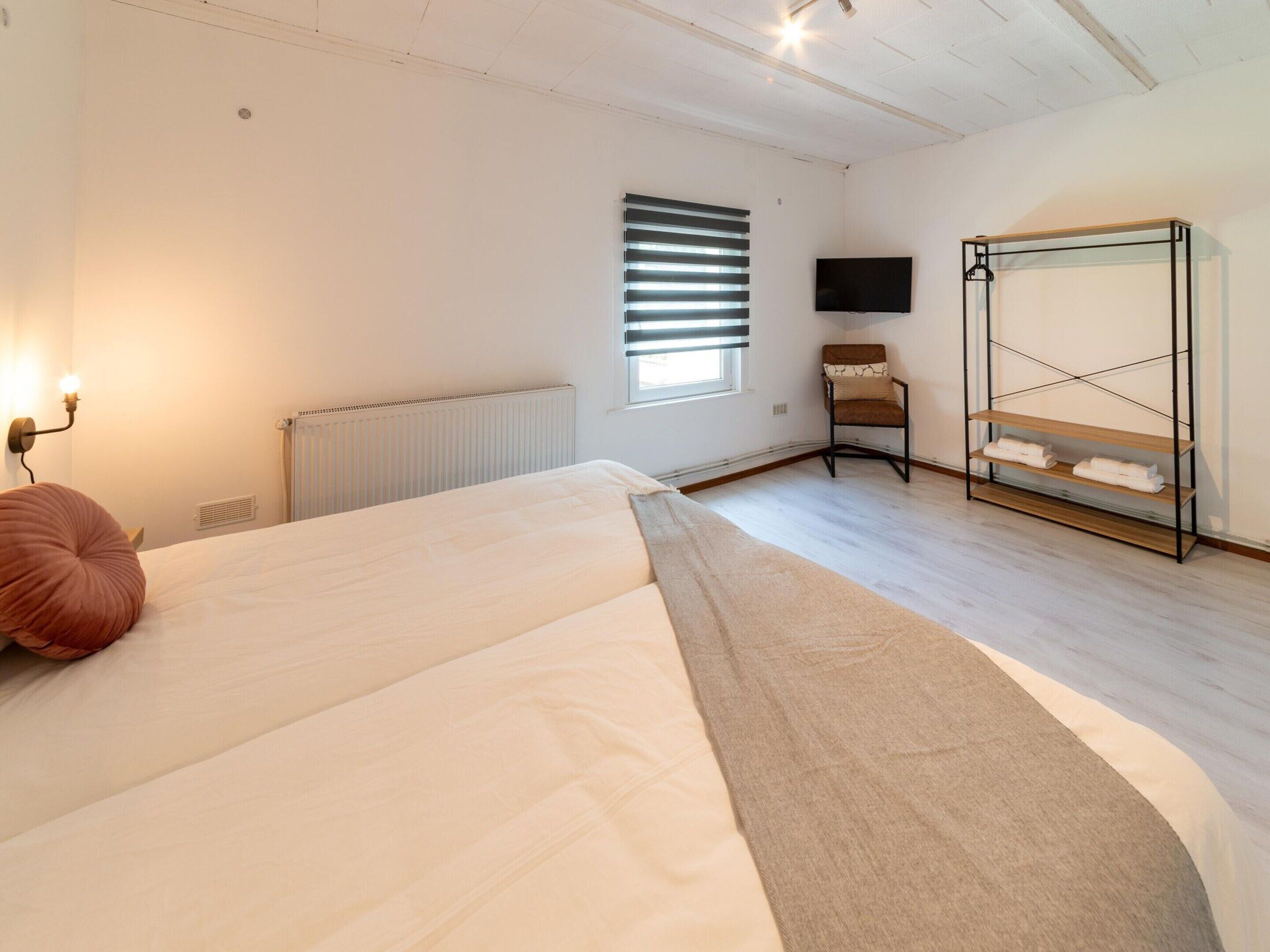 A bedroom with a bed, a chair, a TV, and a radiator.
