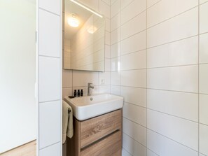 A modern bathroom with a white sink, wooden cabinet, and a mirror above the sink. - Luxe Stay With Sauna & Garden (Scherpenisse)