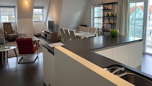 Ein modernes Wohnzimmer mit Essbereich, einer Küche mit integrierter Kochinsel und einem großen Fenster mit Blick nach draußen.