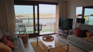 Un salon comprenant un canapé, une table basse, un téléviseur et offrant une vue sur une étendue d’eau grâce à de grandes fenêtres.