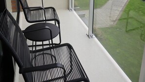 Un balcon avec deux chaises en métal noir et une petite table, donnant sur une zone herbeuse et un chantier de construction où se trouve un camion jaune.