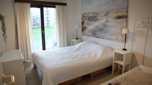 Une chambre d’hôtel avec un grand lit, une table de chevet avec une lampe, un petit bureau et une vue sur un espace verdoyant par la fenêtre.