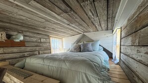 Een rustieke slaapkamer met een groot bed, houten wanden en een schuin dak.