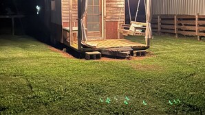 Een klein, laag houten gebouw met een veranda en een schommel, omgeven door een omheinde tuin.