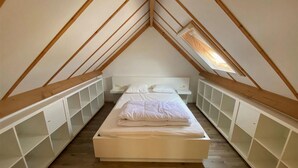 Ein kleines, schmales Schlafzimmer im Dachgeschoss mit schrägen Wänden und Holzbalken. Es hat ein Einzelbett mit weißer Bettwäsche sowie zwei Nachttische.