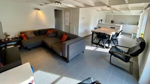 Ein modernes Wohnzimmer mit einem Ecksofa, einem Esstisch mit Stühlen und einer Küche im Hintergrund.