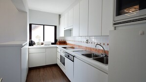 Uma cozinha compacta com armários brancos, uma pia de aço inoxidável e uma janela que traz luz natural.