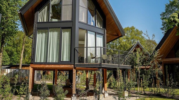 Eine moderne, zweistöckige Holzhütte mit großen Fenstern und einer Holzterrasse.
