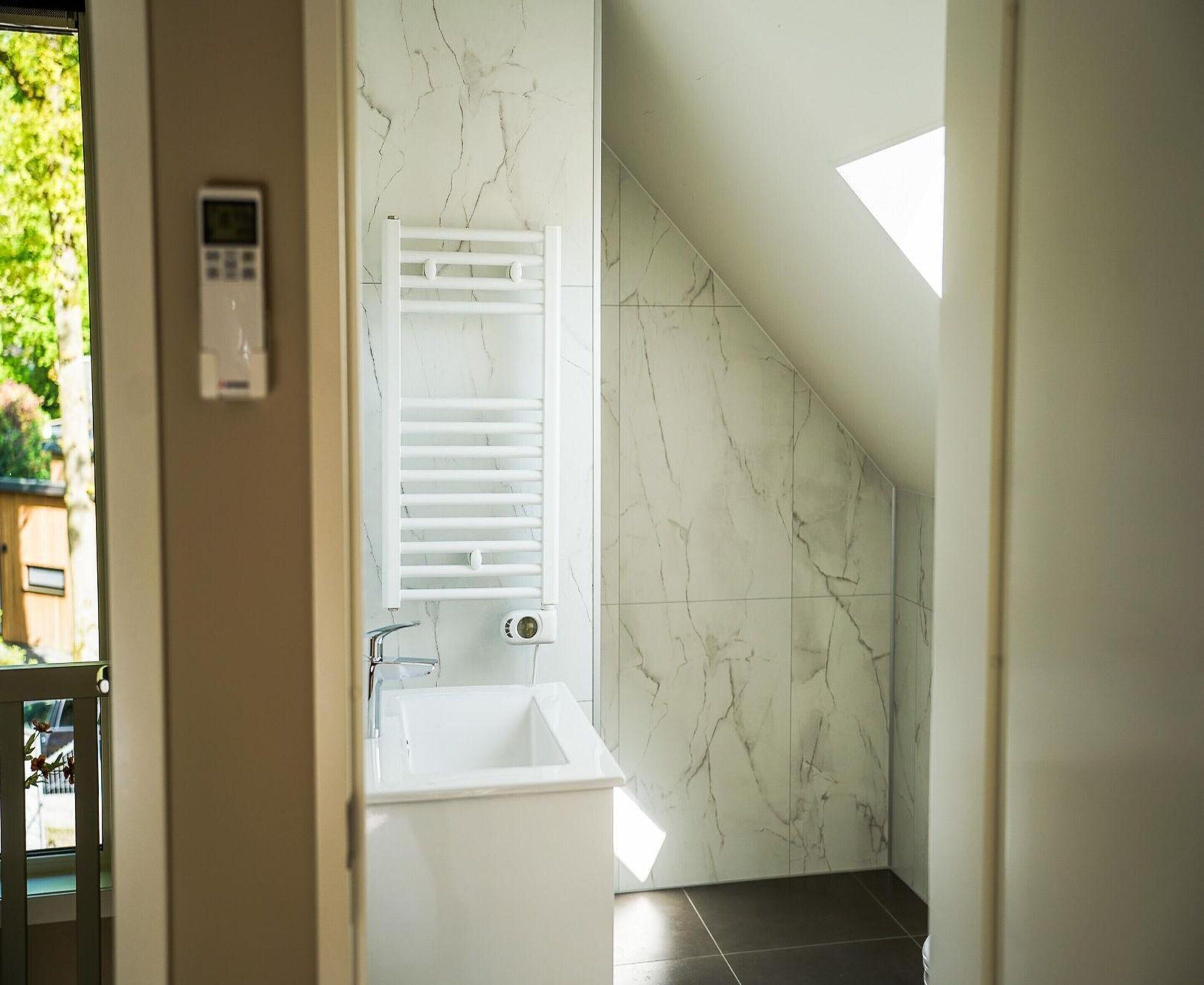 A bathroom with a white bathtub, a towel rack, and a control panel on the wall.