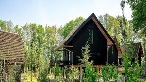 Ein modernes Haus mit dunkler Fassade, einem geneigten Dach und einem sichtbaren Schornstein. Das Anwesen ist von einem gepflegten Garten mit verschiedenen Pflanzen und einer Rasenfläche umgeben.