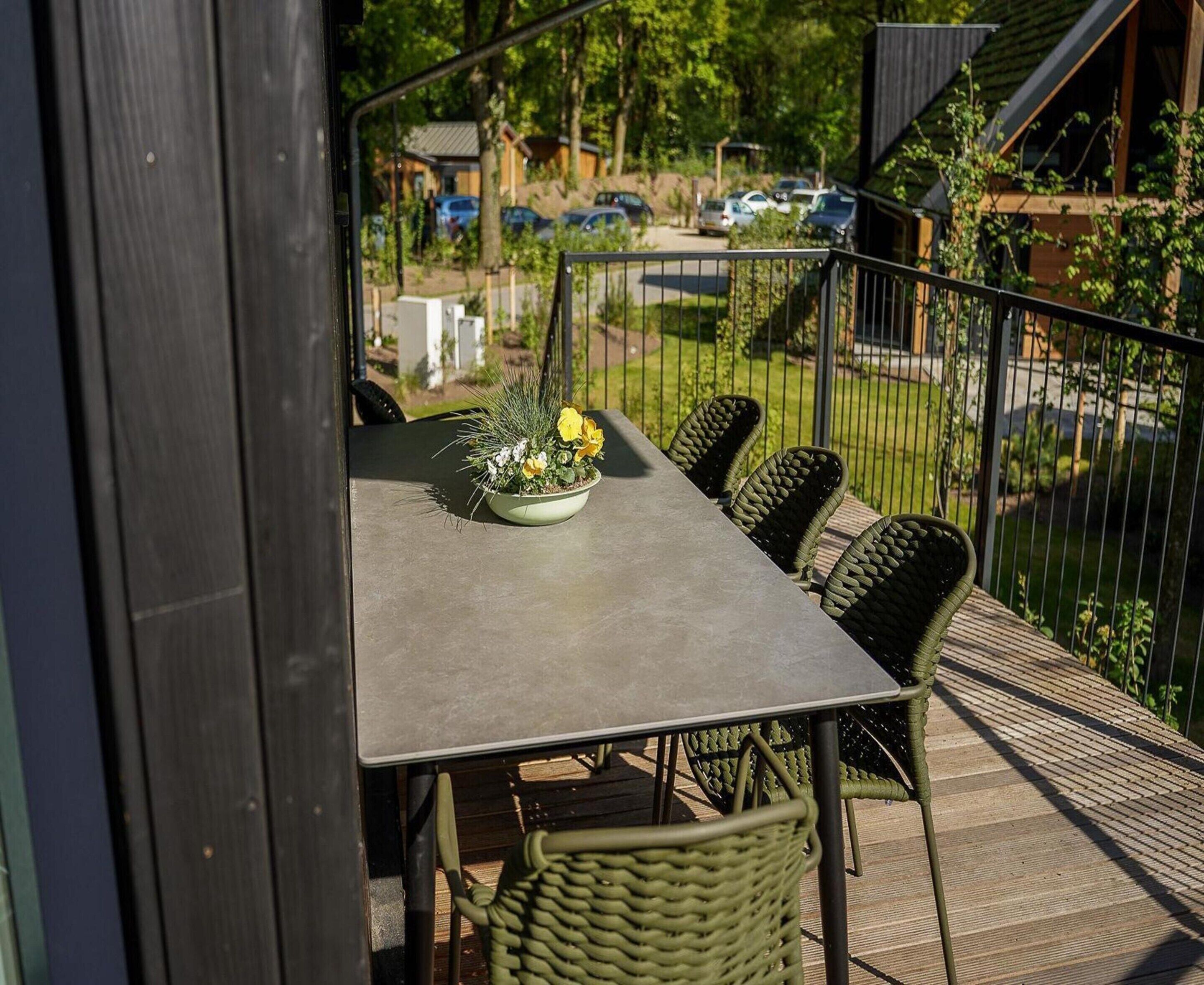 An outdoor dining area with a table and chairs, a potted plant, and a view of a parking lot and buildings in the background.