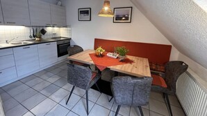 A modern kitchen with white cabinets, a wooden dining table, and a red accent wall. - Bernsteinfinder 4.17 Comfortable Holiday Residence (Zingst)