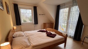 A bedroom with a wooden bed, two windows with curtains, a wooden dresser, and a lamp. - Bernsteinfinder 4.17 Comfortable Holiday Residence (Zingst)