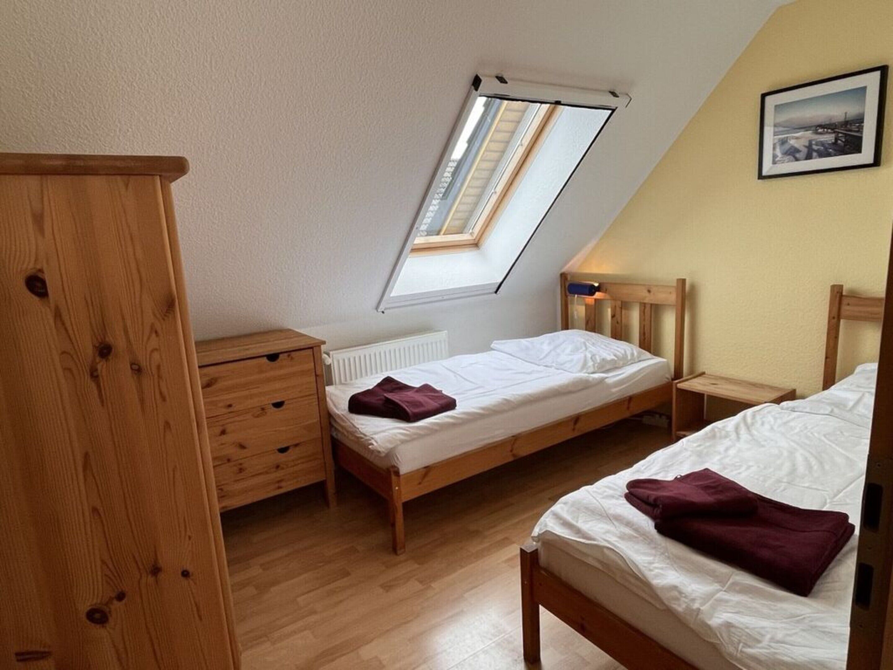 Ein Schlafzimmer mit zwei Betten, einer Holzkommode, einem Oberlicht und einem gerahmten Bild an der Wand.