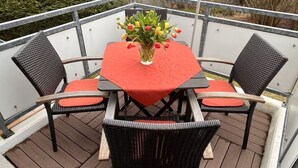 A balcony with a table and four chairs, a vase with flowers, and a view of the surrounding area. - Bernsteinfinder 4.17 Comfortable Holiday Residence (Zingst)