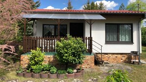 Ein kleines Haus mit rotem Dach, einer hölzernen Veranda und einem Backsteinsockel.