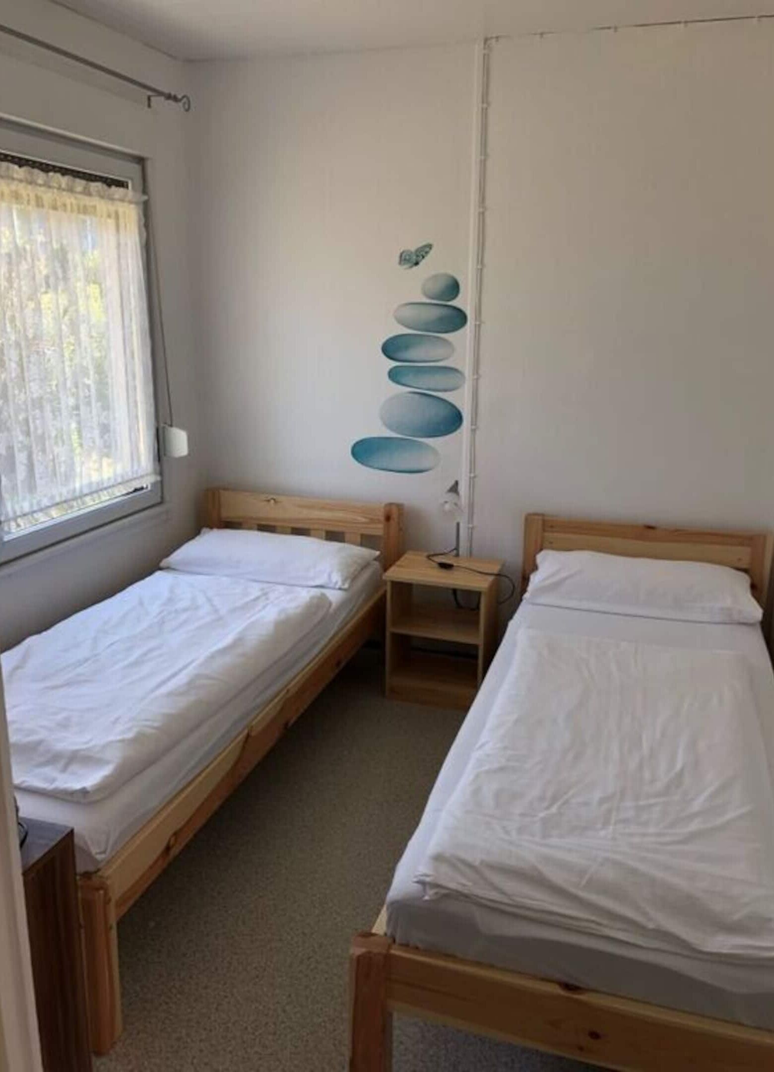 A room with two single beds, a window with curtains, and a wall decoration.