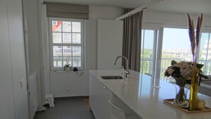 A modern kitchen with a large island, a window with a view, and a potted plant on the windowsill. - Apartment in Nieuwpoort Near the Beach (Nieuwpoort)
