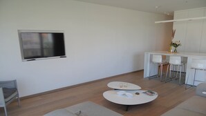 A modern living room with a sofa, two round tables, a TV mounted on the wall, and a small bar area with stools. - Apartment in Nieuwpoort Near the Beach (Nieuwpoort)