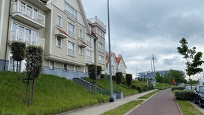 A residential building with multiple balconies, a paved pathway, and a street with parked cars. - Apartment in Nieuwpoort Near the Beach (Nieuwpoort)