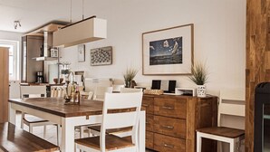 A modern kitchen with white cabinetry, a wooden dining table, and chairs. There is a black stove on the right, a potted plant, and a framed picture on the wall. - Our-island-scharbeutz (Scharbeutz)