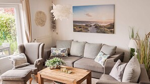 A modern living room with a grey sofa, a wooden coffee table, and a view of the outdoors through a large window. - Our-island-scharbeutz (Scharbeutz)