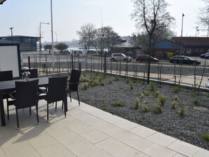 An outdoor patio area with a table and chairs, a gravel garden, and a view of a road with cars and buildings in the background. - High End Travemunde Comfortable Vacation Home (Lübeck)