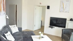 A modern living room with a grey sectional sofa, a white coffee table, and a flat-screen TV mounted on the wall. - High End Travemunde Comfortable Vacation Home (Lübeck)