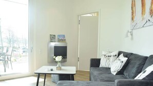 A modern living room with a grey sofa, a small white table, and a TV mounted on the wall. - High End Travemunde Comfortable Vacation Home (Lübeck)