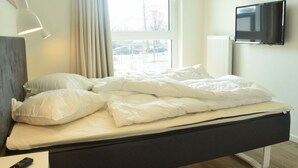 A modern hotel room with a bed, a TV mounted on the wall, and a window with curtains. - High End Travemunde Comfortable Vacation Home (Lübeck)