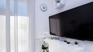 A modern living room with a large flat-screen TV, white console, and potted plants. - Cosy Apartment in Pag (Pag)