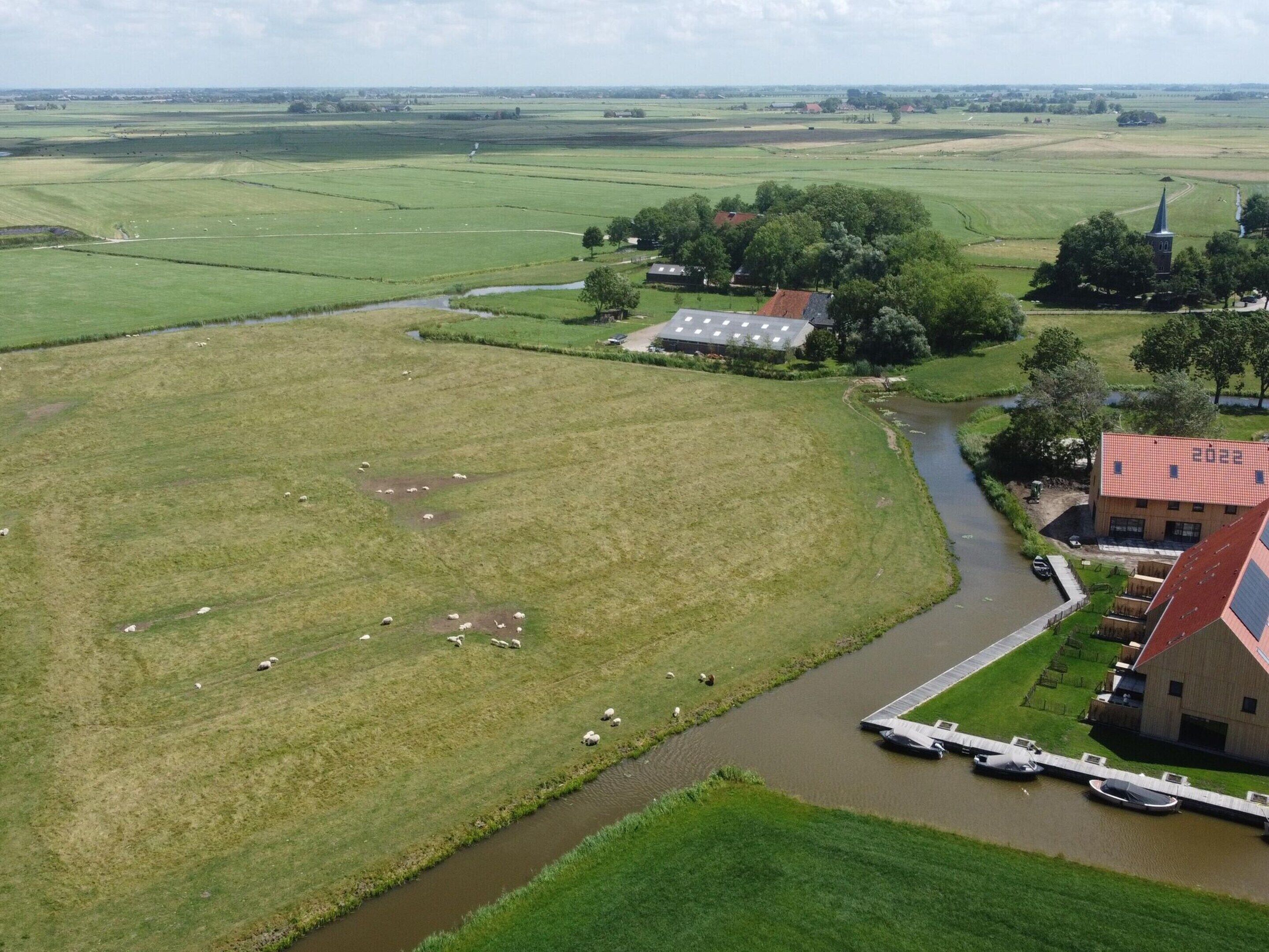 Vista aerea di un paesaggio rurale con campi, un fiume e un edificio con tetto rosso.