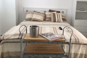 A neatly made bed with striped bedding, a magazine, a remote control, and a metal tray table.