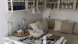 A dining area with a white table set for two, featuring a clear glass pitcher, a white bowl, and a wooden board with cutlery. - Apartment Oleander (Novalja)
