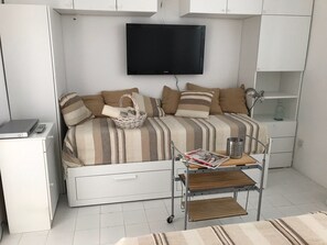 A compact bedroom with a bed, a TV, a desk, and a shelf.