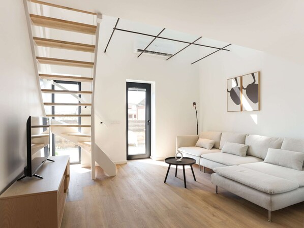 A modern living room with a staircase, a sofa, a coffee table, and a TV. - Suite in Kamperland Near Beach (Kamperland)