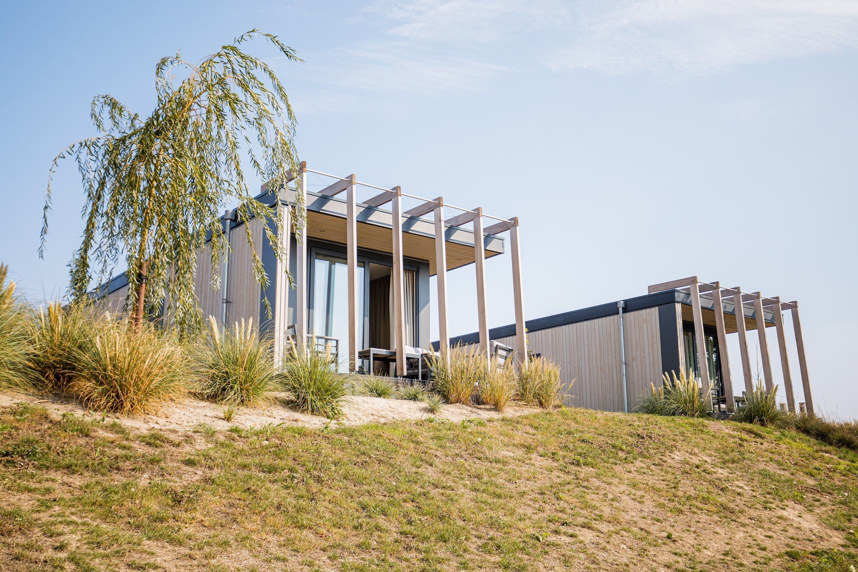 A modern building with a flat roof, large windows, and a wooden structure on the side.