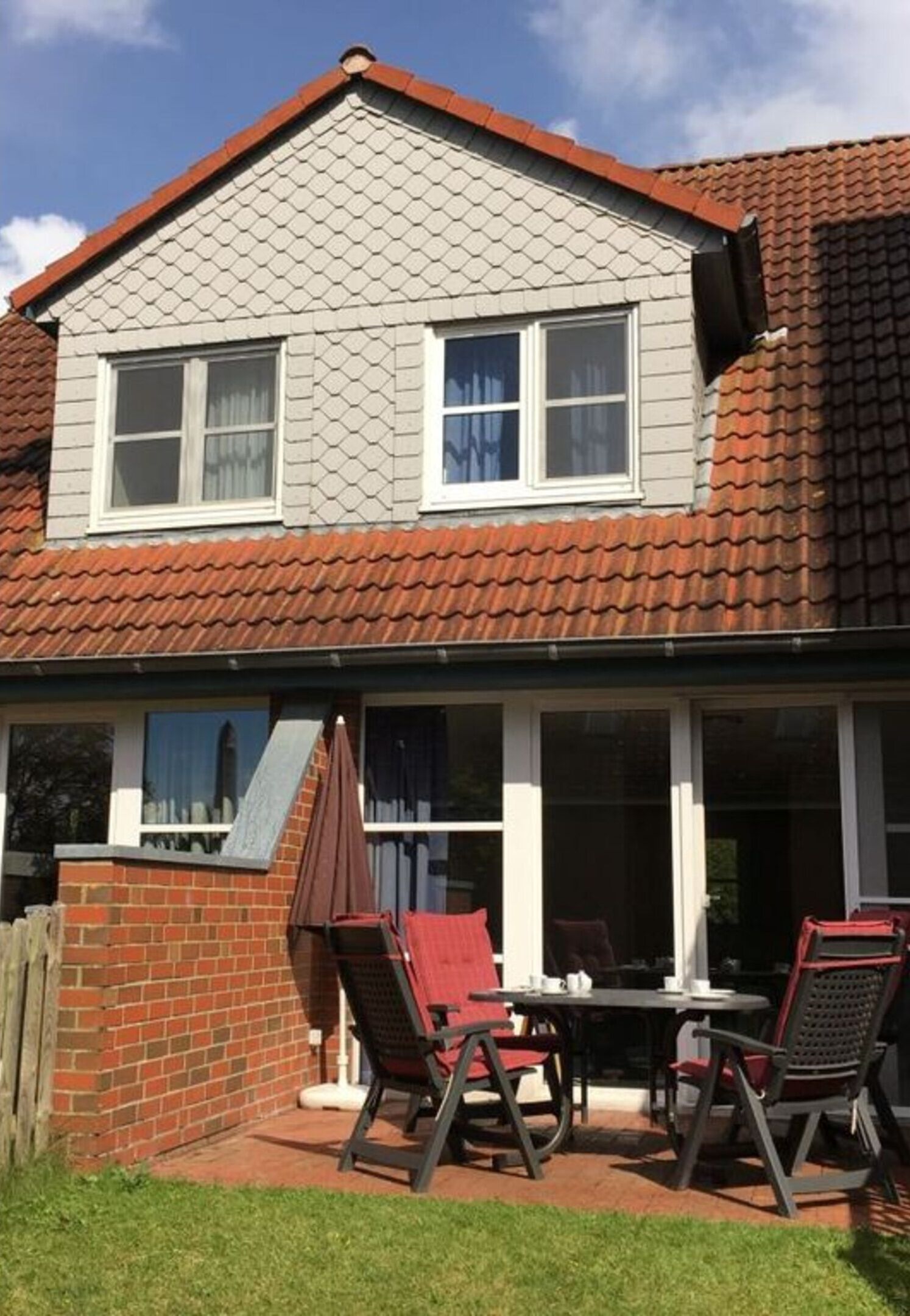 A two-story house with a red-tiled roof, a brick exterior, and a covered patio with a table and chairs.