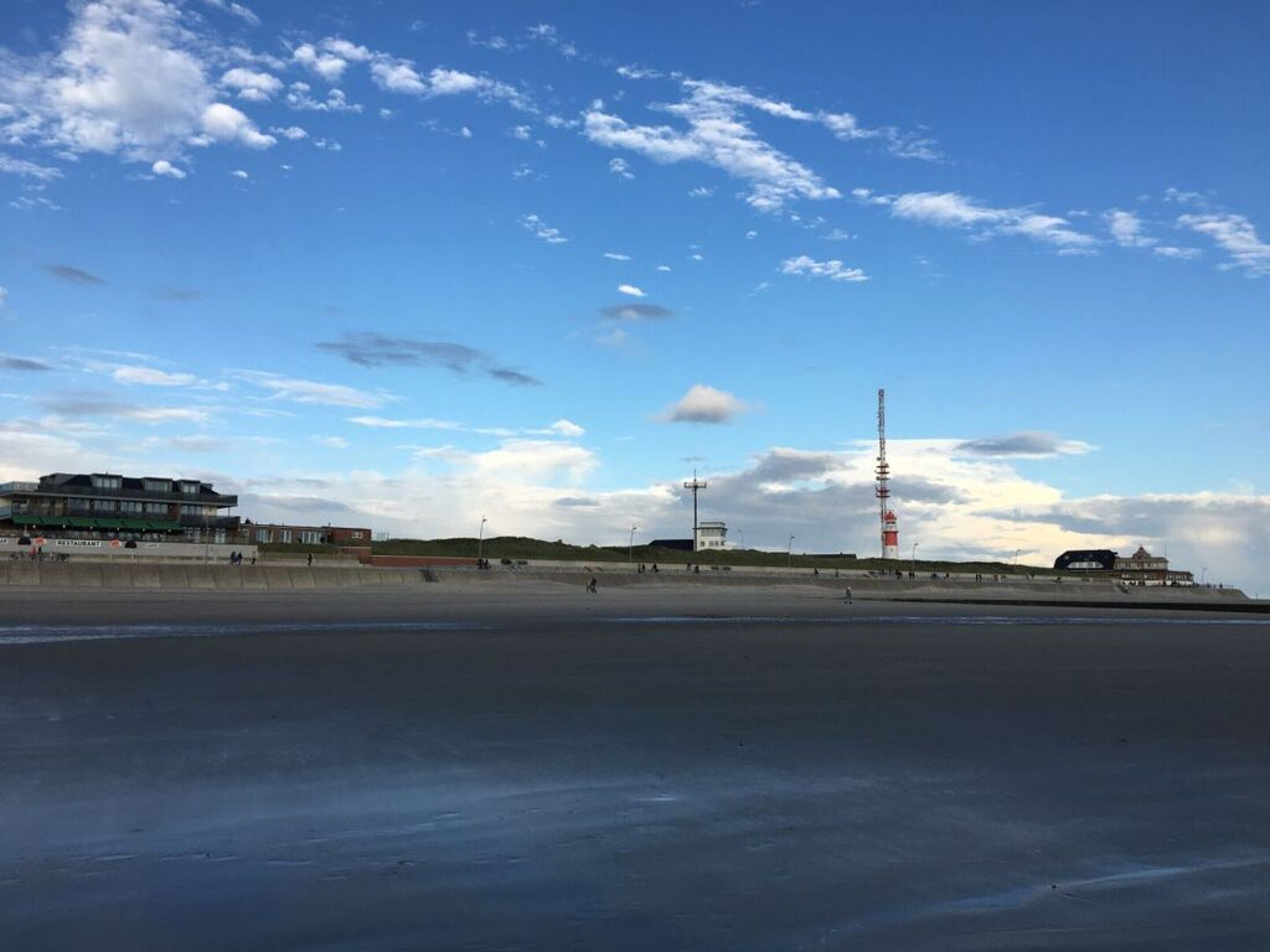 Eine Küstenlandschaft mit Strand, einem hohen Funkturm und einem Gebäude mit rotem Dach.
