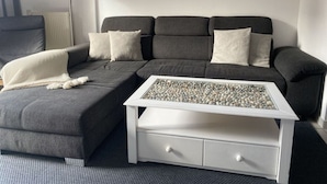 Un salon moderne avec un canapé d’angle gris, une table basse blanche et un lampadaire.