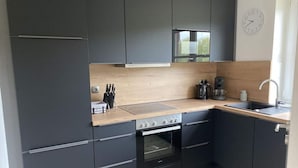 Une cuisine moderne avec des meubles de couleur sombre, un plan de travail en bois, un four encastré et un évier.
