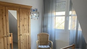 Une chambre avec une armoire en bois, une chaise en osier et un lit avec des oreillers.
