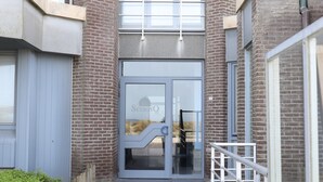 A building entrance with a glass door, a metal staircase, and a brick facade. - Apartment in Nieuwpoort With sea View (Nieuwpoort)