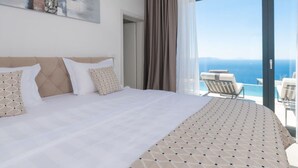 Ett hotellrum med en stor säng, utsikt över havet och en balkong med stolar.