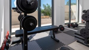 Ett gym med utrustning för styrketräning, en bänk och stora fönster med utsikt över omgivningen.