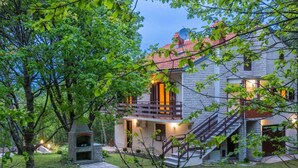 Ein zweistöckiges Haus mit Naturstein-Fassade, einem Balkon mit Holzgeländern und einer Treppe, die zum Obergeschoss führt.