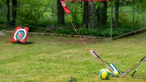 Ein Zielscheibe mit Pfeilen, ein Badminton-Schläger und ein Federball auf einer grünen Wiese.