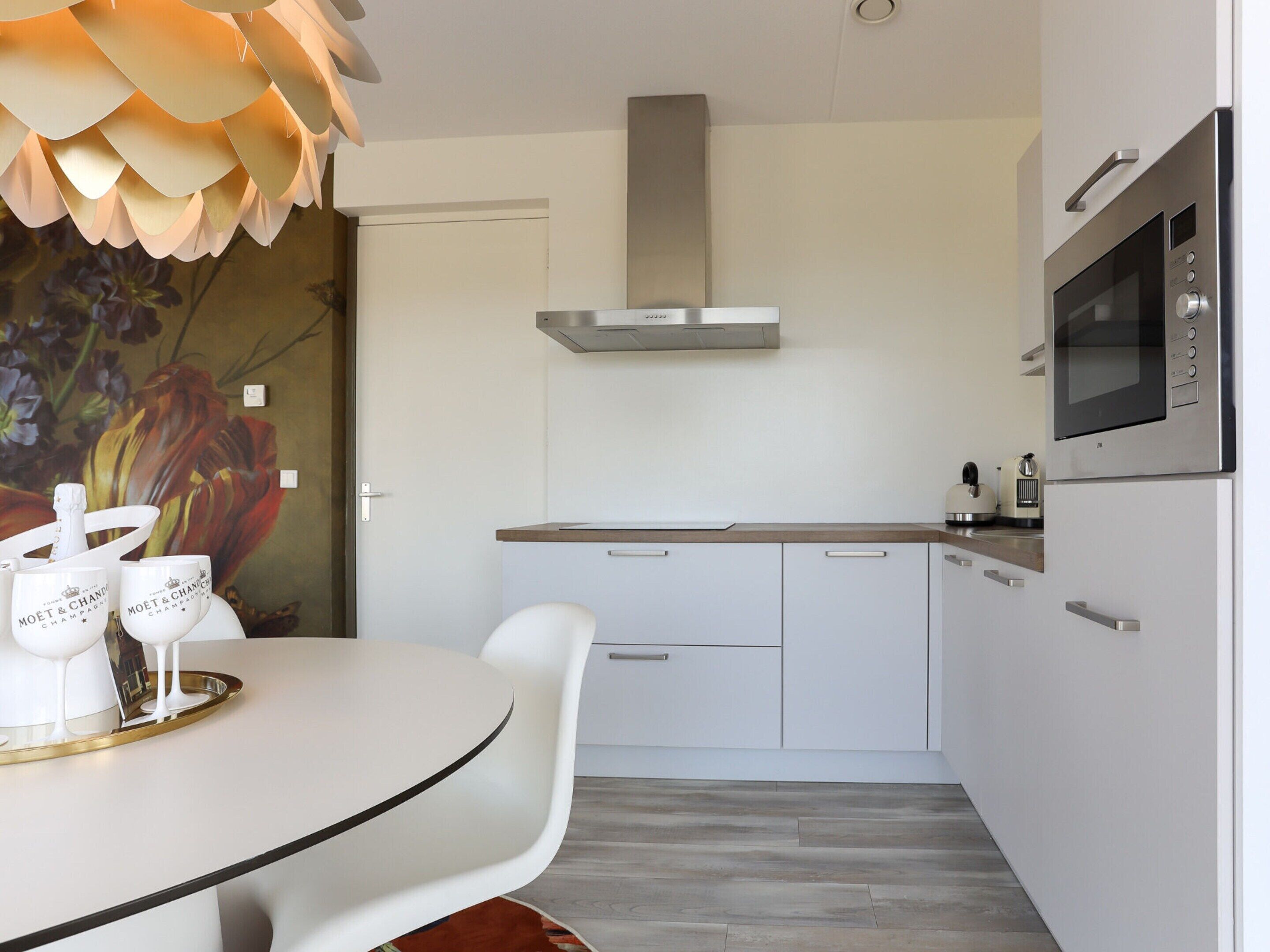 A modern kitchen with white cabinetry, a stainless steel range hood, a microwave, and a dining area with a white table and chairs.