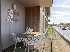 Un balcón con una mesa y sillas, un cartel que dice "Cocktails & Dreams" y vistas a barcos en el agua.